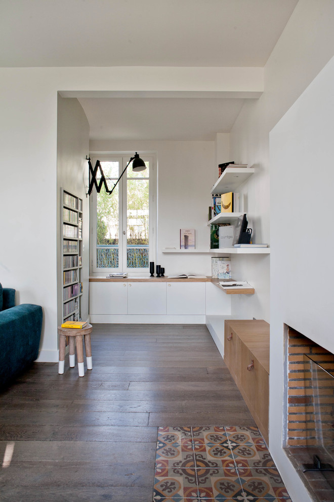 Ejemplo de despacho actual de tamaño medio con paredes blancas, suelo de madera oscura, todas las chimeneas y escritorio empotrado