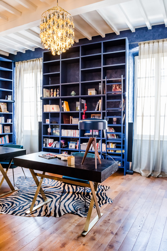 Foto de despacho bohemio con biblioteca, paredes azules, suelo de madera en tonos medios y escritorio independiente