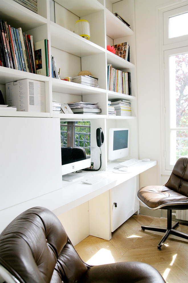 Diseño de despacho actual grande con paredes blancas, suelo de madera clara y escritorio empotrado