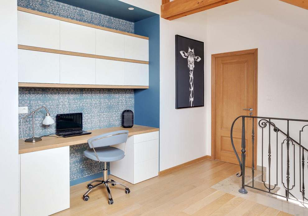 Foto på ett stort eklektiskt arbetsrum, med vita väggar, ljust trägolv och ett inbyggt skrivbord