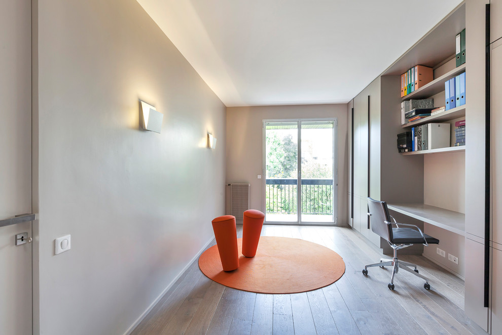 Cette image montre un bureau design de taille moyenne avec une bibliothèque ou un coin lecture, un mur beige, parquet foncé, un bureau intégré et un sol beige.