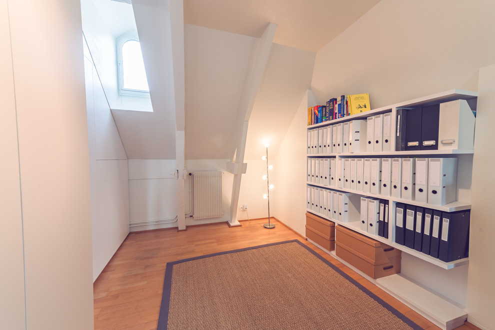 Exempel på ett litet modernt hemmabibliotek, med vita väggar, ljust trägolv och ett fristående skrivbord