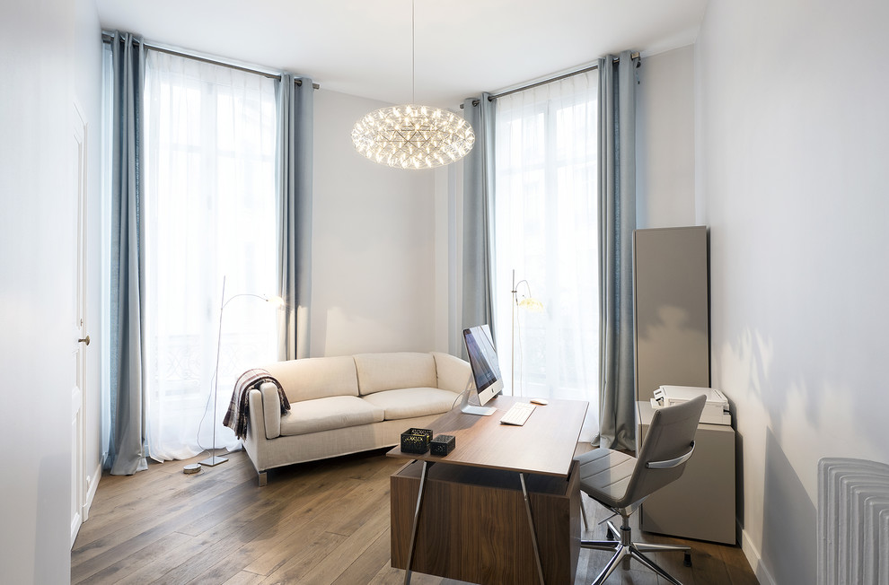 This is an example of a large contemporary study in Paris with white walls, laminate floors, a freestanding desk and brown floors.