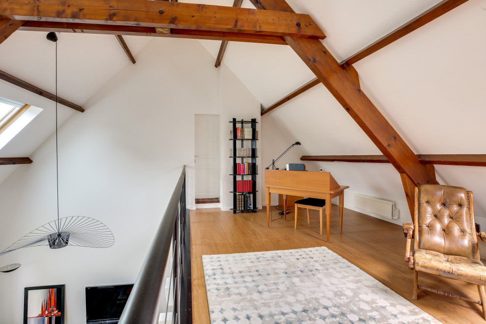 Modernes Arbeitszimmer mit weißer Wandfarbe, braunem Holzboden, freistehendem Schreibtisch, braunem Boden, freigelegten Dachbalken und gewölbter Decke in Sonstige