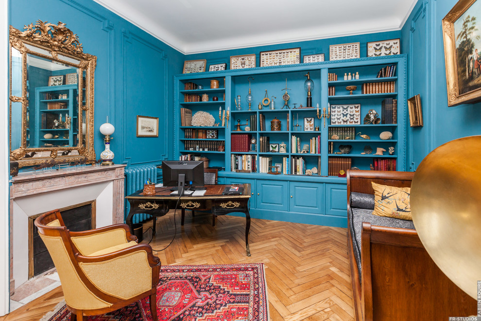 Источник вдохновения для домашнего уюта: большой домашняя библиотека в викторианском стиле с синими стенами, светлым паркетным полом, стандартным камином, фасадом камина из камня и отдельно стоящим рабочим столом