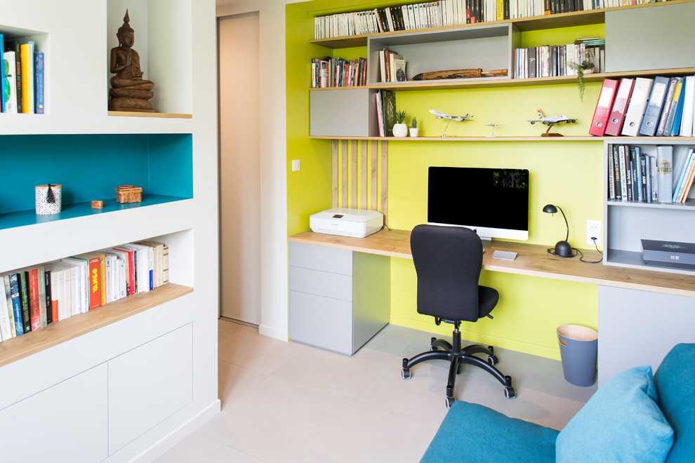 Cette image montre un bureau design de taille moyenne avec une bibliothèque ou un coin lecture, un mur vert, un bureau intégré et un sol gris.