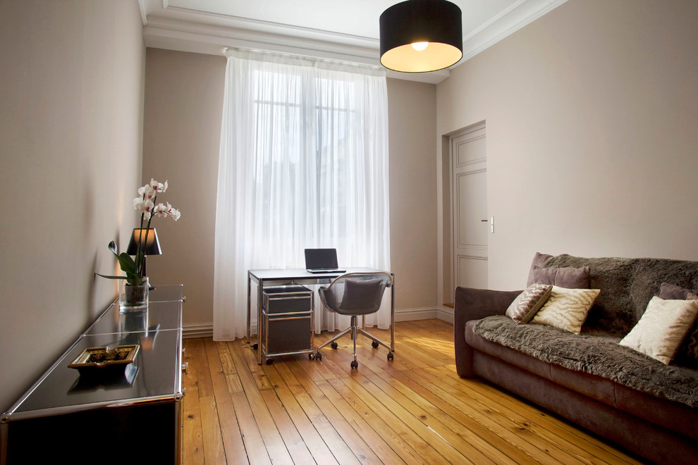Imagen de despacho actual de tamaño medio con paredes beige, suelo de madera en tonos medios y escritorio independiente