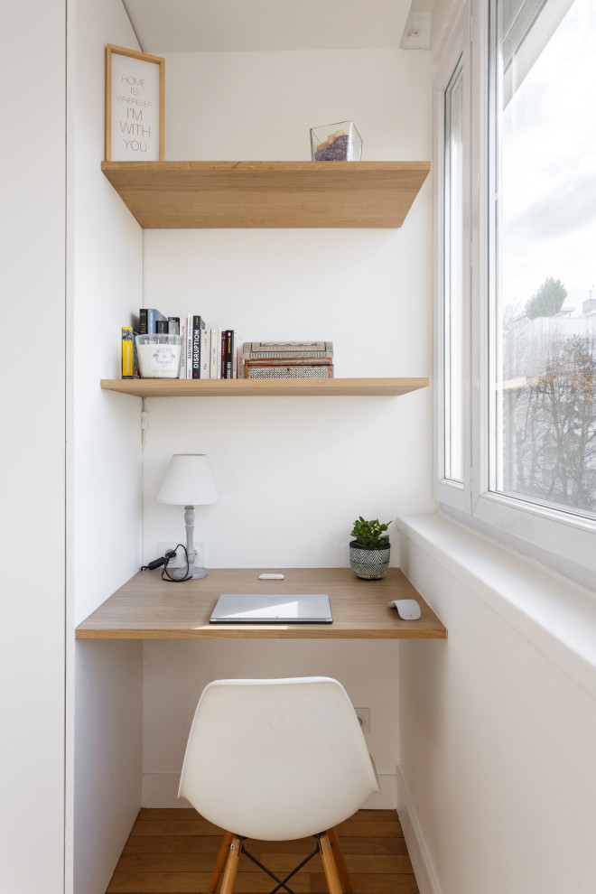 Foto på ett litet skandinaviskt hemmabibliotek, med vita väggar, mellanmörkt trägolv och ett inbyggt skrivbord