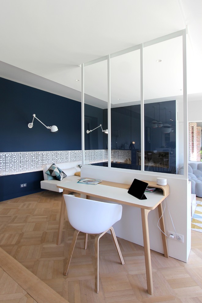 Пример оригинального дизайна: рабочее место в современном стиле с синими стенами, светлым паркетным полом, отдельно стоящим рабочим столом и стандартным камином