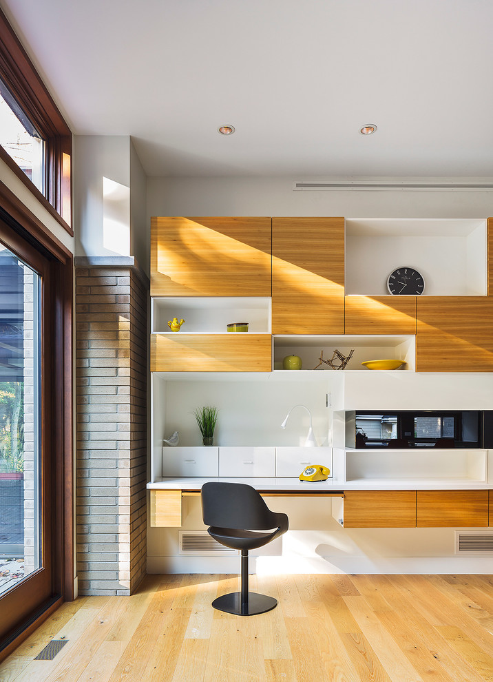 Kleines Modernes Arbeitszimmer ohne Kamin mit Arbeitsplatz, hellem Holzboden, Kaminumrandung aus Holz und Einbau-Schreibtisch in Montreal