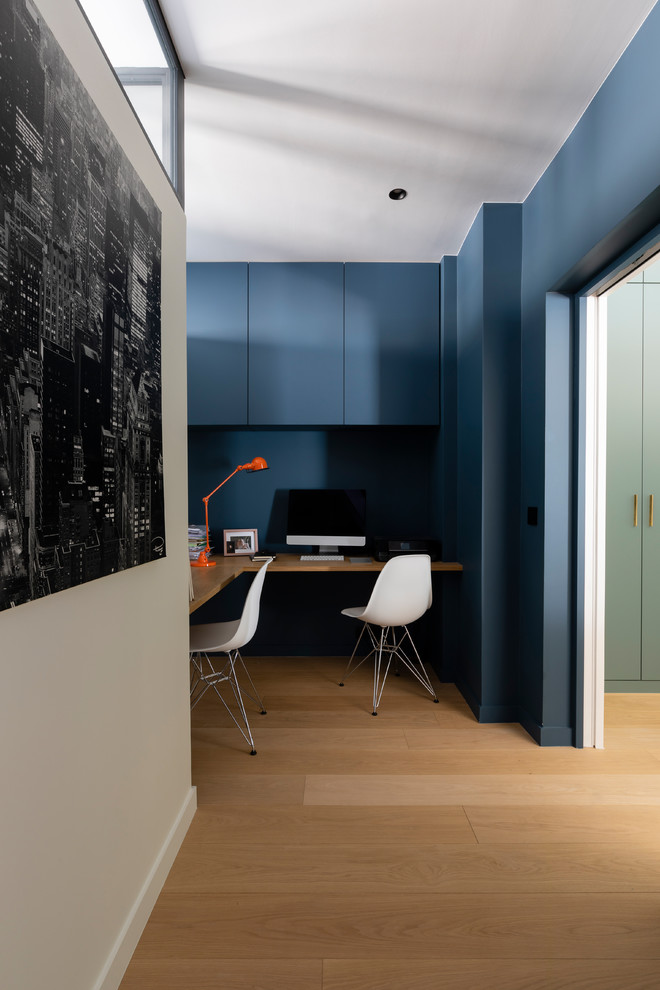 Mittelgroßes Modernes Arbeitszimmer mit Arbeitsplatz, blauer Wandfarbe, hellem Holzboden und Einbau-Schreibtisch in Paris