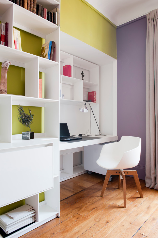 Réalisation d'un bureau design avec un sol en bois brun, un bureau intégré et un mur multicolore.