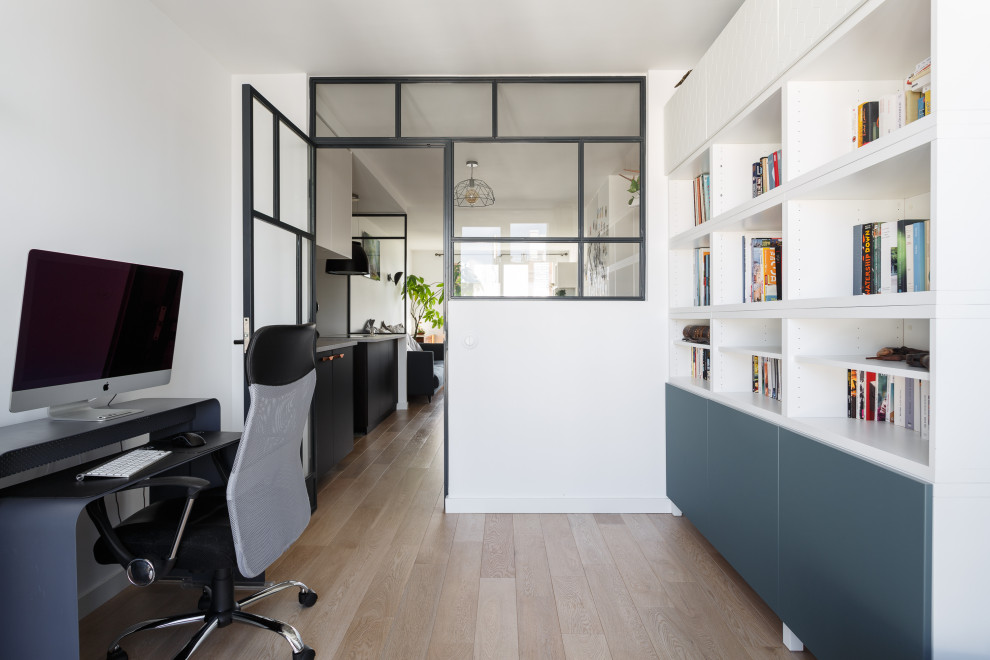 Cette image montre un bureau design de taille moyenne avec une bibliothèque ou un coin lecture, un mur blanc, parquet clair, aucune cheminée, un bureau indépendant et un sol beige.