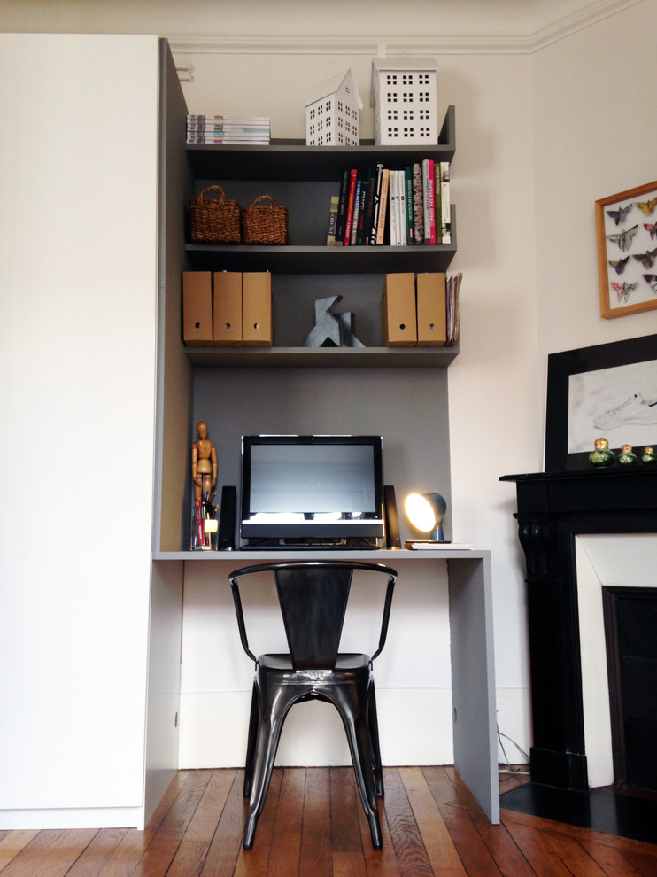 Diseño de despacho actual pequeño con paredes grises, suelo de madera clara, chimenea de esquina y escritorio empotrado