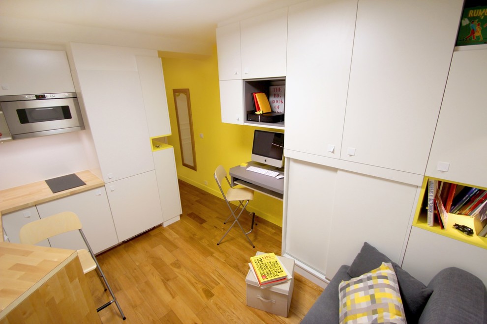 Inspiration för små moderna hemmabibliotek, med gula väggar, mellanmörkt trägolv och ett inbyggt skrivbord