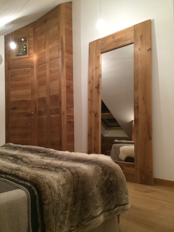 This is an example of a large rustic master bedroom in Turin with white walls, light hardwood flooring and no fireplace.