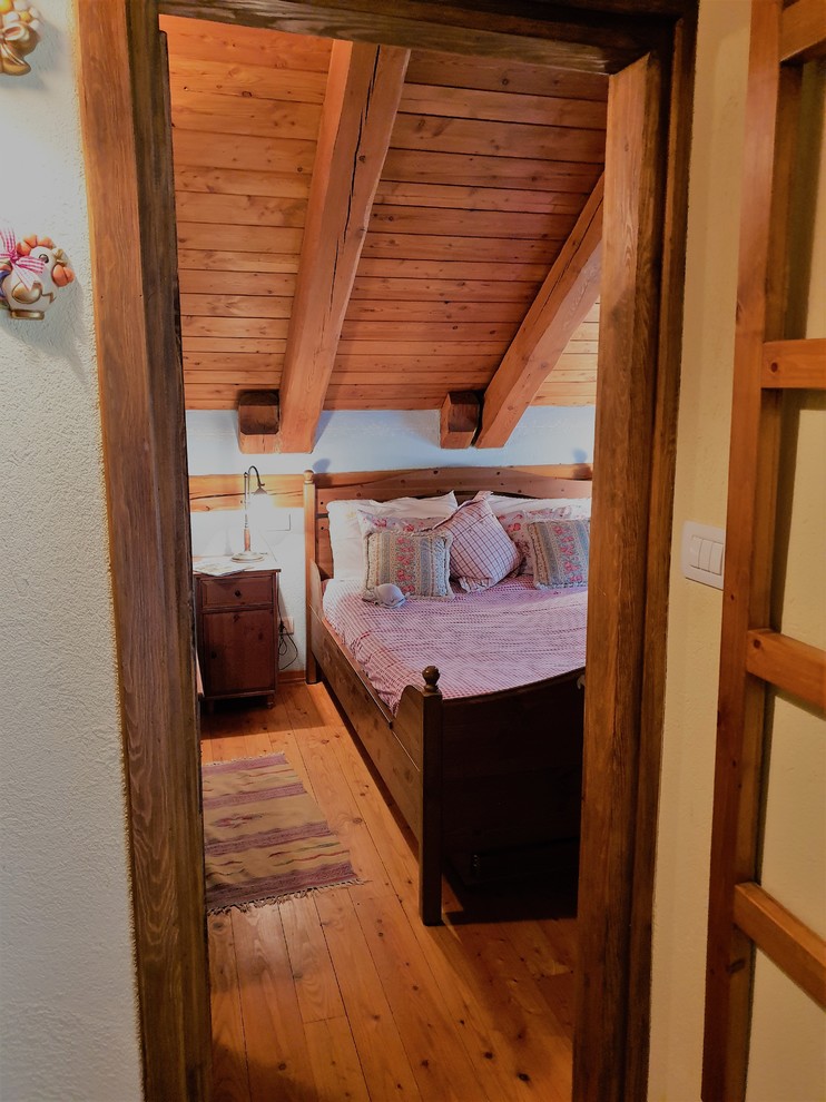 Foto de dormitorio rural pequeño con paredes amarillas, suelo de madera clara, estufa de leña, marco de chimenea de metal y suelo marrón