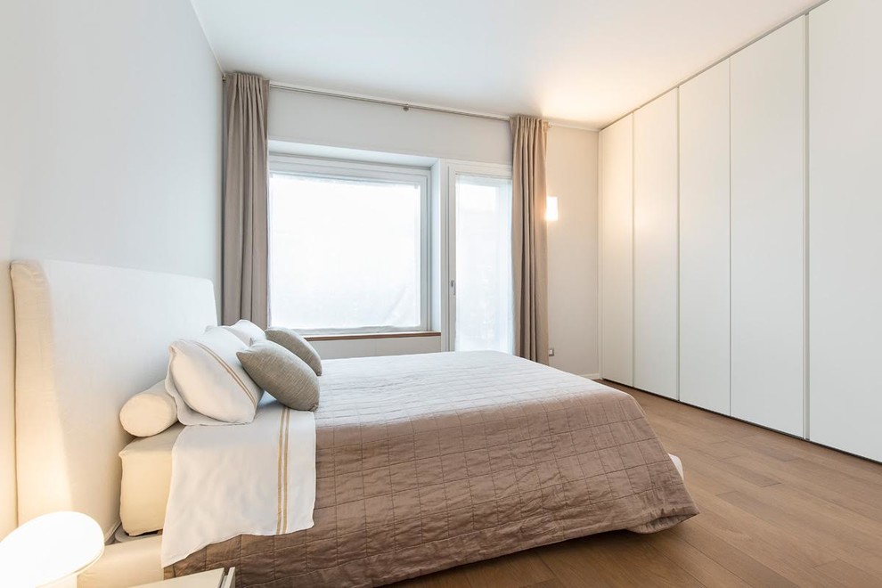 Photo of a contemporary master bedroom in Milan with white walls, medium hardwood flooring, no fireplace and brown floors.