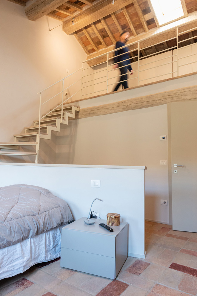 Ejemplo de dormitorio tipo loft rústico de tamaño medio sin chimenea con paredes beige, suelo de baldosas de terracota y suelo multicolor