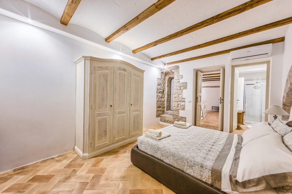 Réalisation d'une chambre parentale tradition de taille moyenne avec un mur blanc et tomettes au sol.
