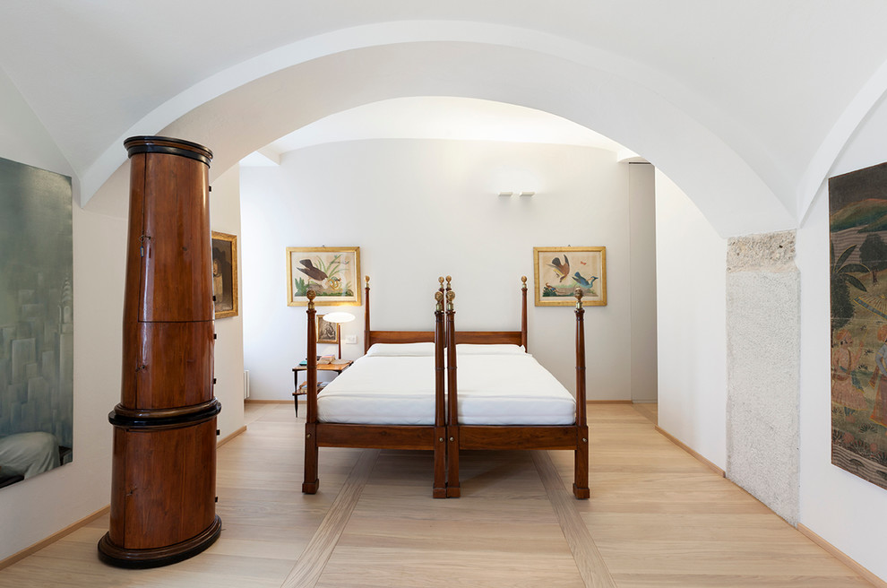 Ejemplo de dormitorio principal mediterráneo con paredes blancas, suelo de madera clara, estufa de leña y marco de chimenea de metal