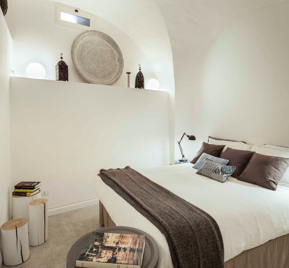 Modelo de dormitorio tipo loft costero con paredes blancas, suelo de baldosas de porcelana y suelo beige