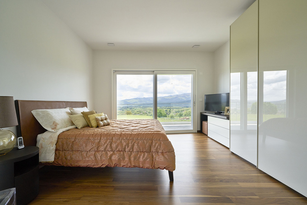 Modelo de dormitorio principal contemporáneo con paredes blancas, suelo de madera en tonos medios y suelo marrón