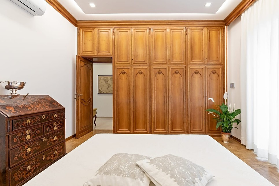 Modelo de dormitorio principal tradicional grande sin chimenea con paredes blancas, suelo de madera en tonos medios y suelo marrón