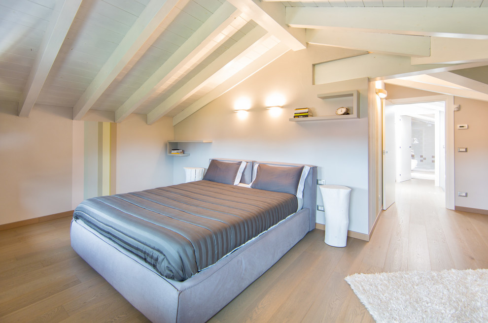 Imagen de dormitorio actual con paredes beige, suelo de madera clara y techo inclinado