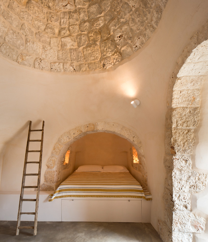 Cette image montre une petite chambre d'amis méditerranéenne avec un mur beige, sol en béton ciré, aucune cheminée et un sol gris.