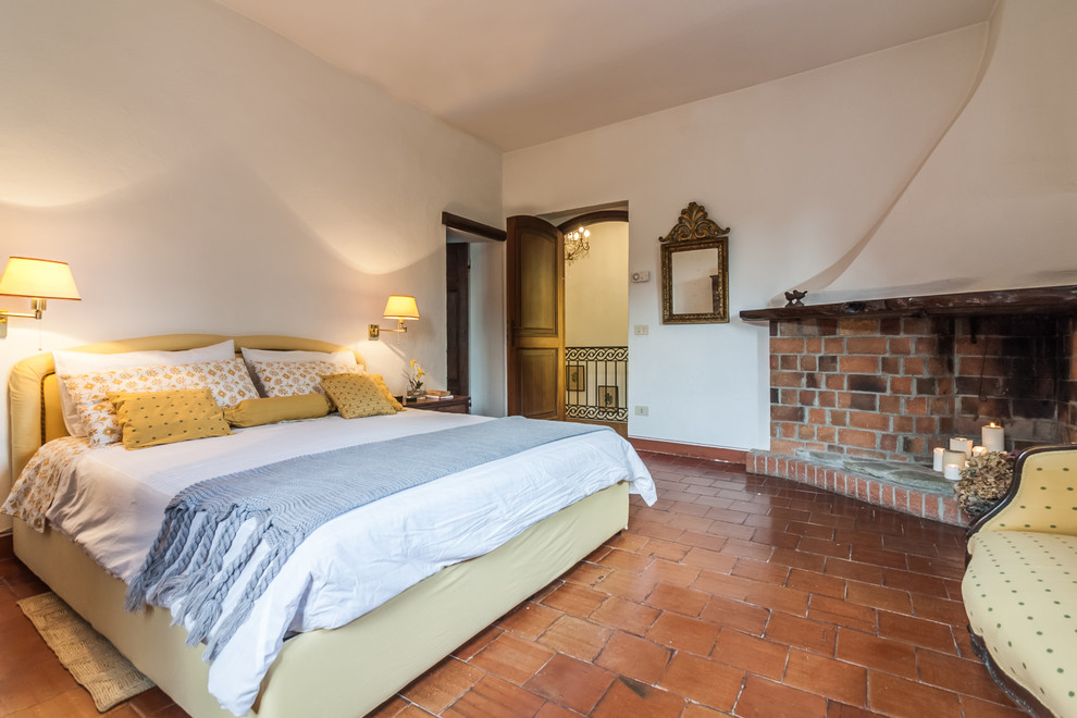 Пример оригинального дизайна: хозяйская спальня в классическом стиле с угловым камином, белыми стенами, полом из терракотовой плитки, фасадом камина из кирпича и коричневым полом