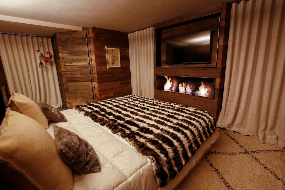 Свежая идея для дизайна: большая хозяйская спальня в стиле рустика с коричневыми стенами, бетонным полом, горизонтальным камином, фасадом камина из дерева и серым полом - отличное фото интерьера