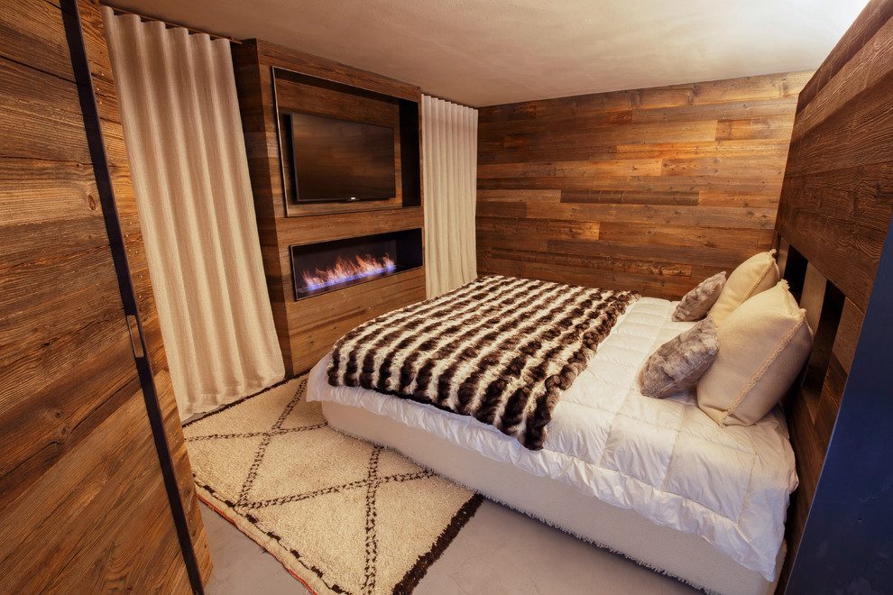 Cette image montre une grande chambre parentale chalet avec un mur marron, sol en béton ciré, une cheminée ribbon, un manteau de cheminée en bois et un sol gris.