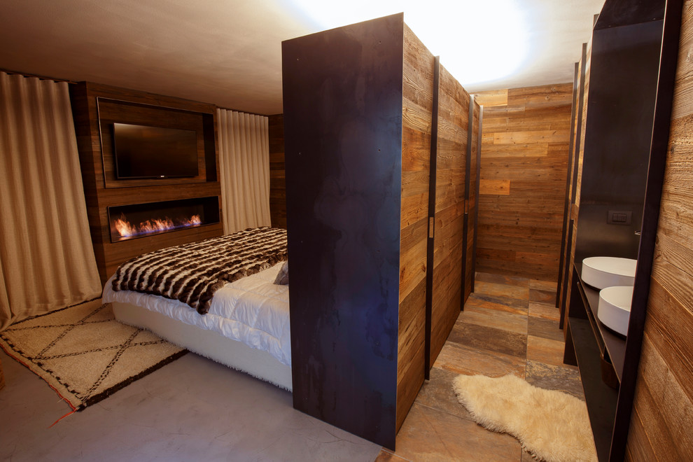 Diseño de dormitorio principal rural grande con paredes marrones, suelo de cemento, chimenea lineal, marco de chimenea de madera y suelo gris