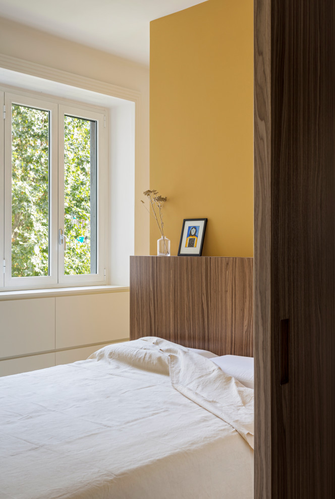 Imagen de dormitorio principal actual pequeño con paredes amarillas, suelo de madera en tonos medios y boiserie