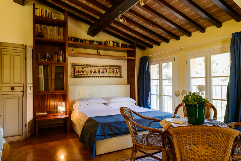 Esempio di una camera da letto mediterranea con pareti gialle, pavimento in legno massello medio e pavimento marrone