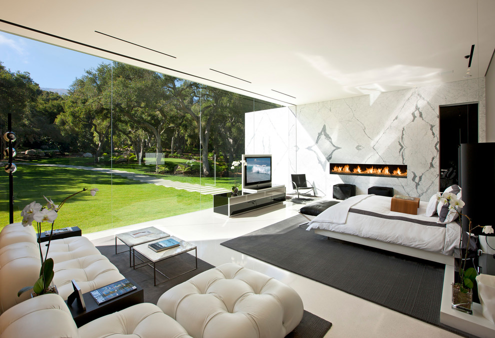 Imagen de dormitorio principal y televisión moderno con paredes blancas, chimenea lineal y marco de chimenea de piedra