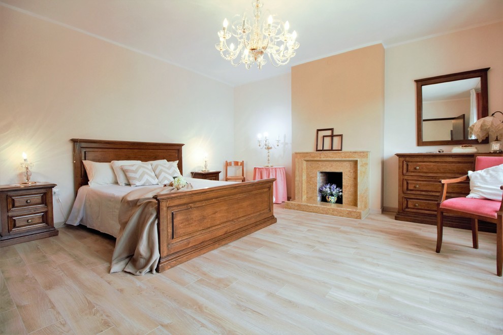 Modelo de dormitorio principal clásico grande con paredes beige, suelo de madera clara, todas las chimeneas y marco de chimenea de piedra