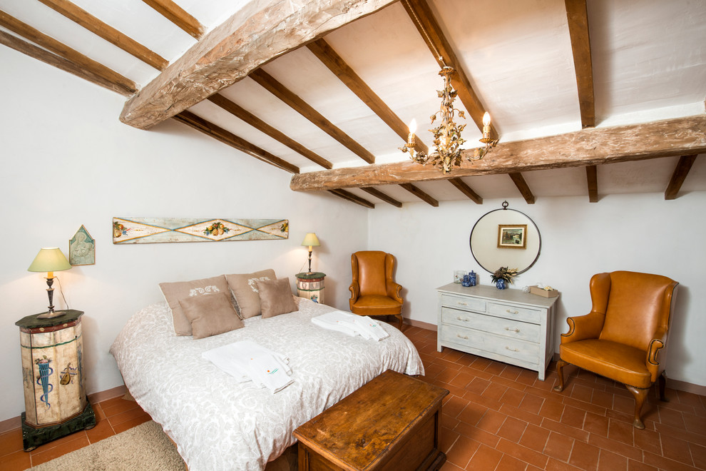 На фото: хозяйская спальня среднего размера в стиле кантри с белыми стенами, полом из терракотовой плитки и коричневым полом