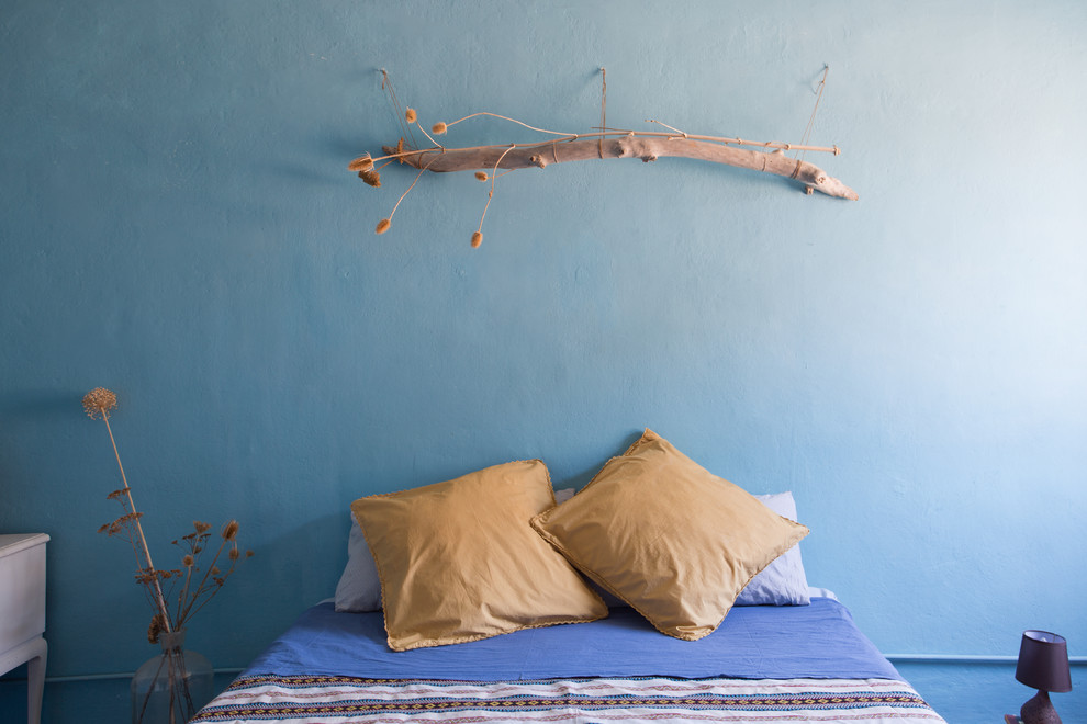 Cette image montre une chambre parentale méditerranéenne avec un mur bleu, tomettes au sol et un sol rouge.