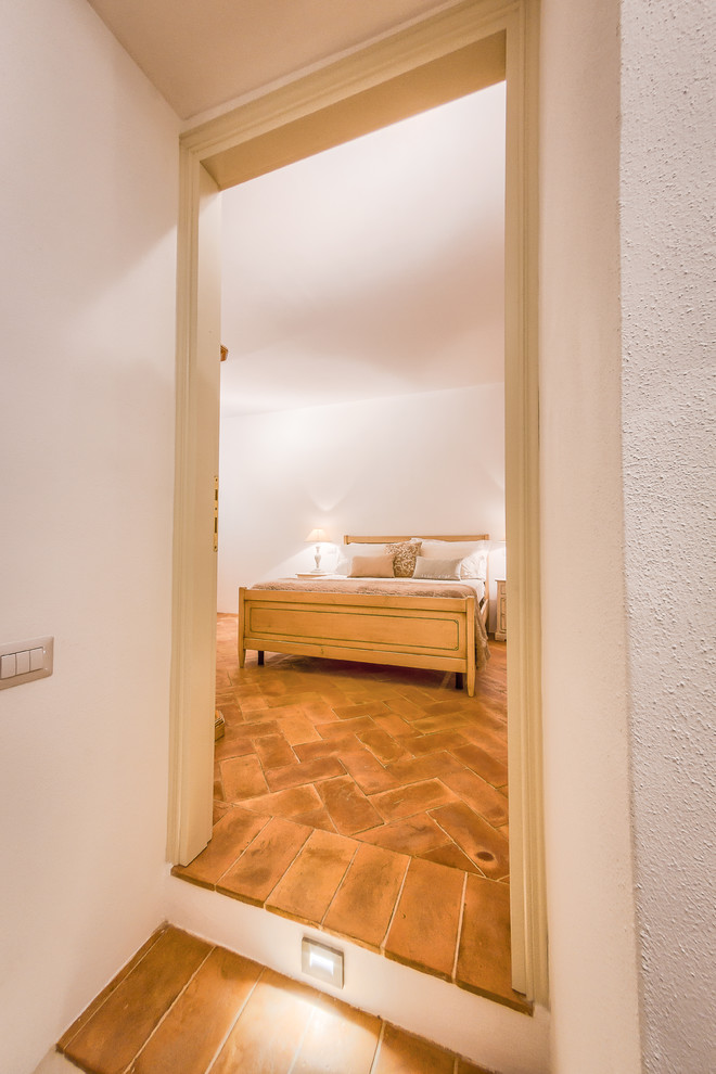 Example of a mid-sized tuscan master terra-cotta tile bedroom design in Other with white walls