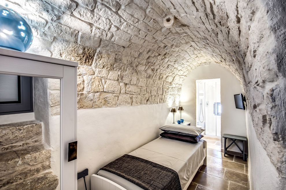 This is an example of a mediterranean guest bedroom in Rome with white walls and brown floors.