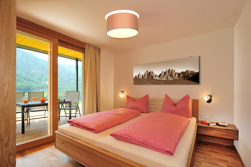 Ejemplo de dormitorio principal actual de tamaño medio sin chimenea con paredes blancas y suelo de madera en tonos medios
