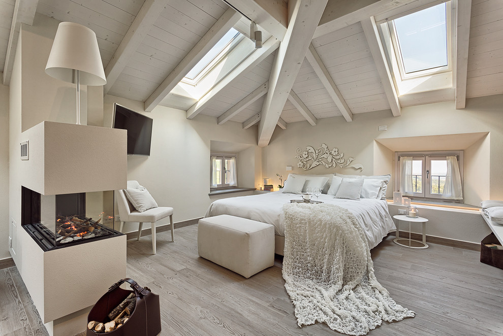 ボローニャにある中くらいなコンテンポラリースタイルのおしゃれな主寝室 (白い壁、淡色無垢フローリング、両方向型暖炉、漆喰の暖炉まわり、グレーの床、勾配天井)