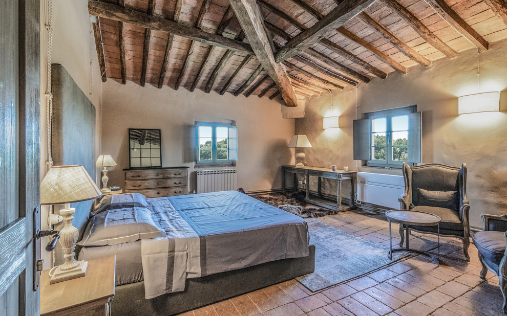 Imagen de dormitorio principal de estilo de casa de campo grande con paredes beige, suelo naranja, vigas vistas y suelo de baldosas de terracota