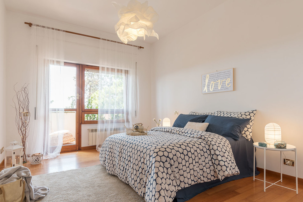 This is an example of a mediterranean guest bedroom in Rome with white walls, medium hardwood flooring and brown floors.