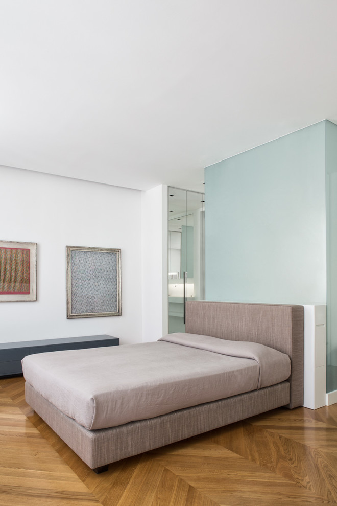 This is an example of a contemporary master bedroom in Milan with white walls and medium hardwood flooring.