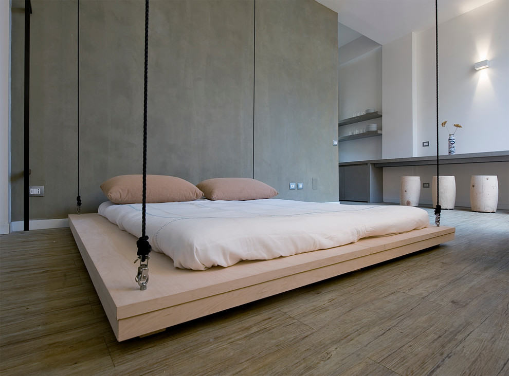 Immagine di una camera matrimoniale industriale con pareti grigie e pavimento in legno massello medio
