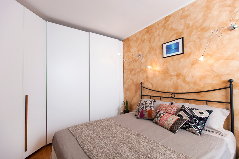 Modelo de dormitorio principal moderno de tamaño medio con parades naranjas y suelo de madera en tonos medios