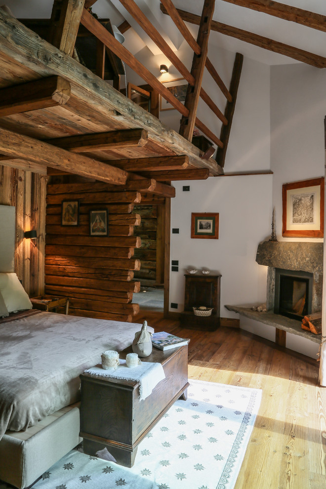 Foto di una camera matrimoniale stile rurale con pareti marroni, pavimento in legno massello medio, camino ad angolo, cornice del camino in pietra e pavimento marrone